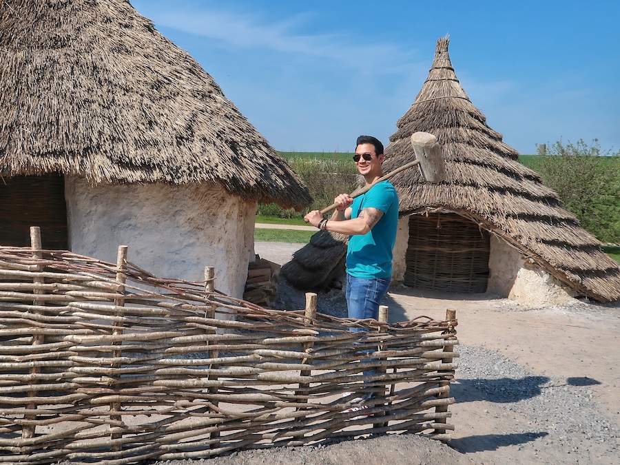 Jeff is exploring the Neolithic houses at Stonehenge carrying a big hammer.