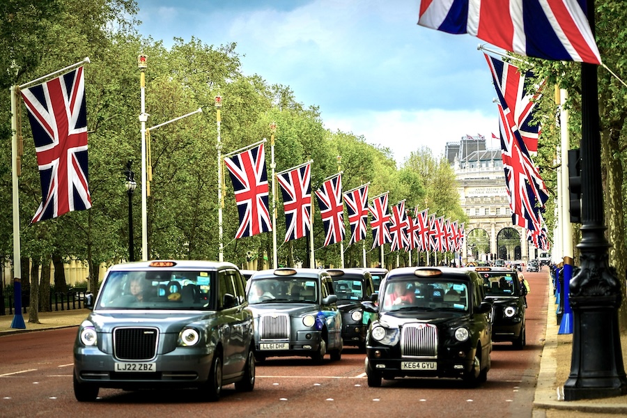 A street is full of black taxis with Union Jack flag lining the sides. Cover image for 