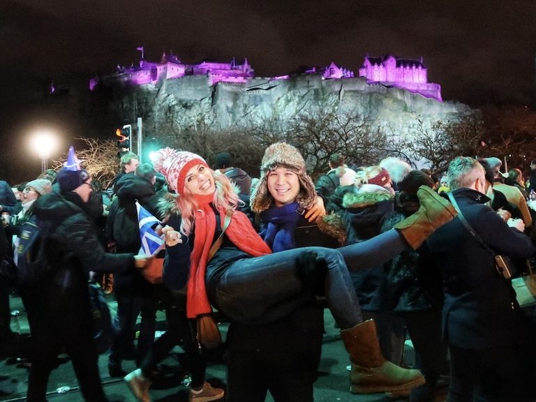 Couple celebrating Hogmanay at Edinburgh's Street Party with Edinburgh Castle illuminated behind them