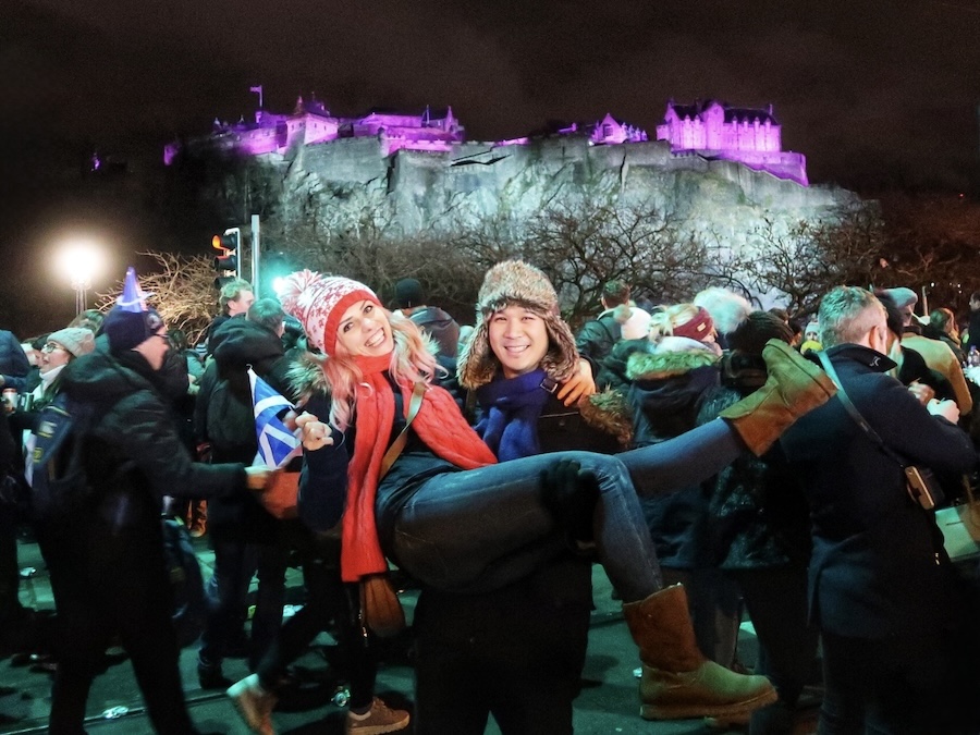 Couple celebrating Hogmanay at Edinburgh's Street Party with Edinburgh Castle illuminated behind them